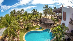 A swimming pool surrounded by palm trees and a thatched-roof structure. - Duro Beach Hotel (Caucaia)