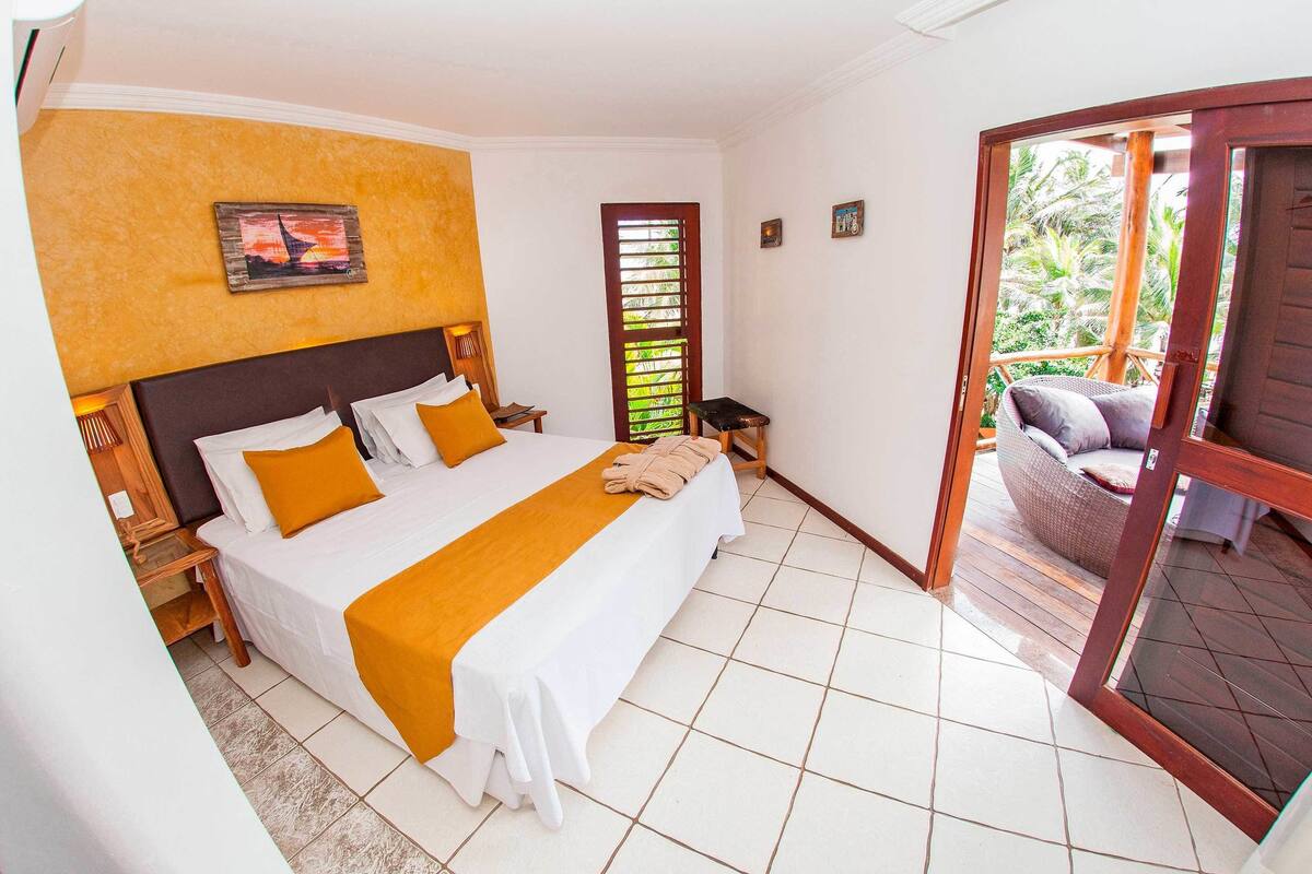A hotel room with a large bed, a wooden headboard, a small table, and a view of the outdoors through a glass door.