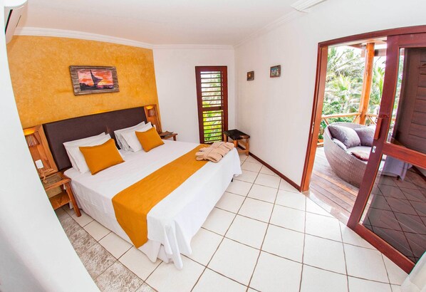 A hotel room with a large bed, a wooden headboard, a small table, and a view of the outdoors through a glass door. - Duro Beach Hotel (Caucaia)