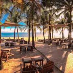 A beachside restaurant with outdoor seating, palm trees, and a view of the ocean. - Duro Beach Hotel (Caucaia)