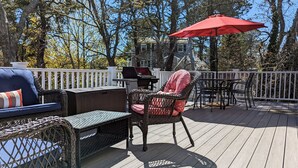 An outdoor deck with wicker furniture, a grill, and a red umbrella.