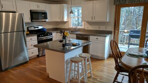 A modern kitchen with white cabinets, stainless steel appliances, and a wooden dining area.