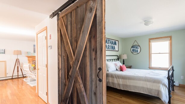 A bedroom with a wooden door, a bed with white bedding, a window, and a wall with a sign.