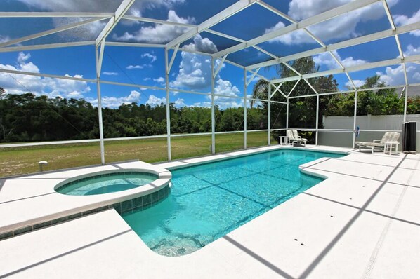 A covered outdoor swimming pool with a hot tub, surrounded by a white fence and a grassy area.