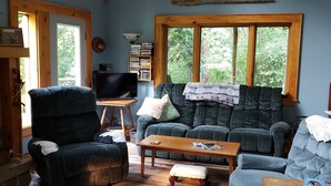 A cozy living room with a large window, a mounted deer head, a blue sofa, a wooden coffee table, and a television.