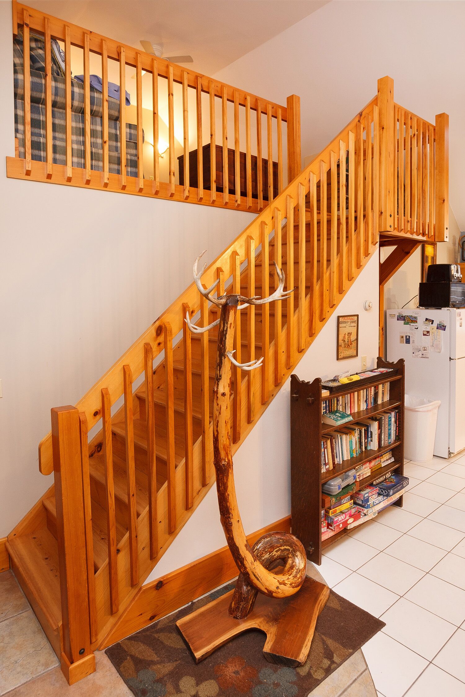 Un escalier en bois au design rustique, un porte-manteau en bois orné de bois de cerf et une bibliothèque remplie de livres.