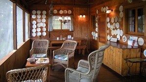 A rustic wooden cabin interior with wicker furniture, a dining table, and a wall adorned with numerous plates.