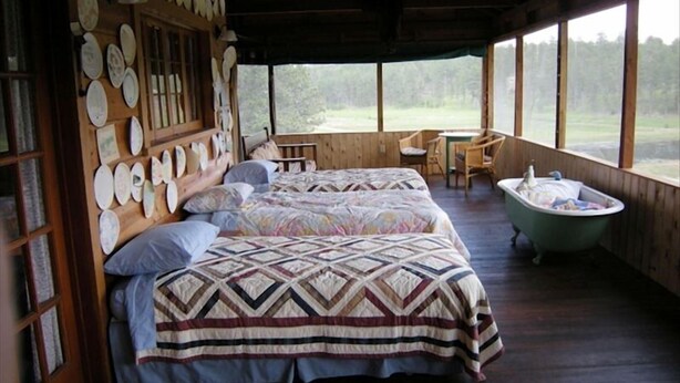 A rustic cabin with two beds, a wooden wall adorned with plates, a wooden table, and a bathtub.