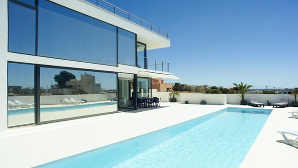 A modern poolside area with a clear blue pool, lounge chairs, and a two-story building with large windows. - Casa Pane (Ibiza Town)