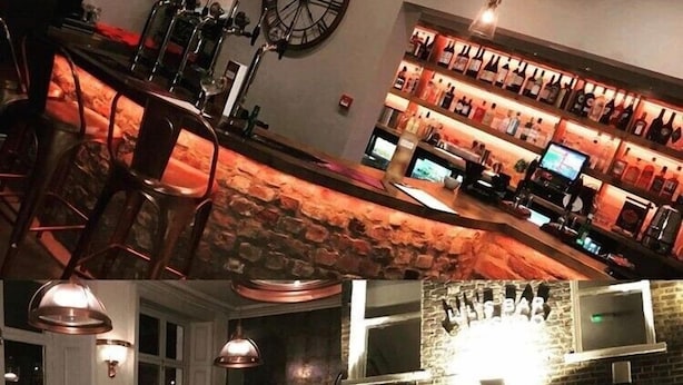 A bar area with a stone wall, a clock, and a wine rack. - Lil's Bar and Bistro (York)