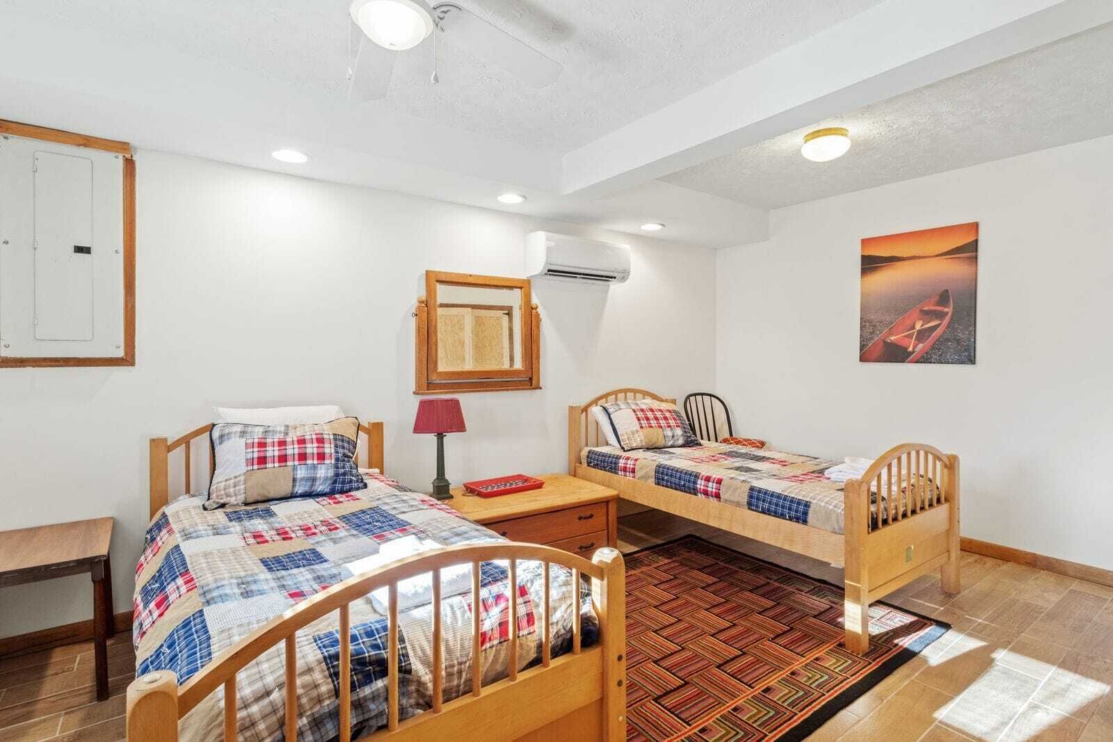 Une chambre à coucher avec deux lits en bois, une lampe rouge, un miroir et un tableau représentant un coucher de soleil sur l’eau.