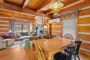 A cozy log cabin interior with a wooden dining table, chairs, a sofa, and a fireplace.