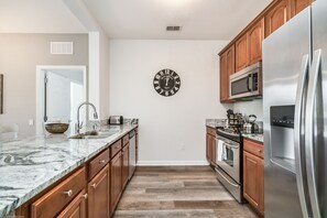 Una cocina moderna con armarios de madera, un refrigerador de acero inoxidable, un microondas y una encimera de mármol.