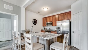 A kitchen with a central island, wooden cabinets, stainless steel appliances, and white chairs. - *BRAND NEW! * CHARMING ORLANDO VISTA CAY  3/BR  2/ FULL BATH CONDO  *SLEEPS 6-8* (Orlando)