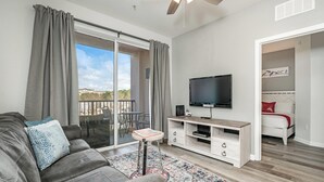 A modern living room with a grey sofa, a flat-screen TV on a wooden stand, a small side table, and a patterned rug. - *BRAND NEW! * CHARMING ORLANDO VISTA CAY  3/BR  2/ FULL BATH CONDO  *SLEEPS 6-8* (Orlando)