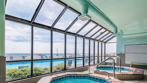 Une piscine intérieure avec vue sur l’océan, un jacuzzi et un toit ouvrant.