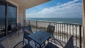 Varanda com mesa e cadeiras, vista para uma praia com cercas e pessoas.