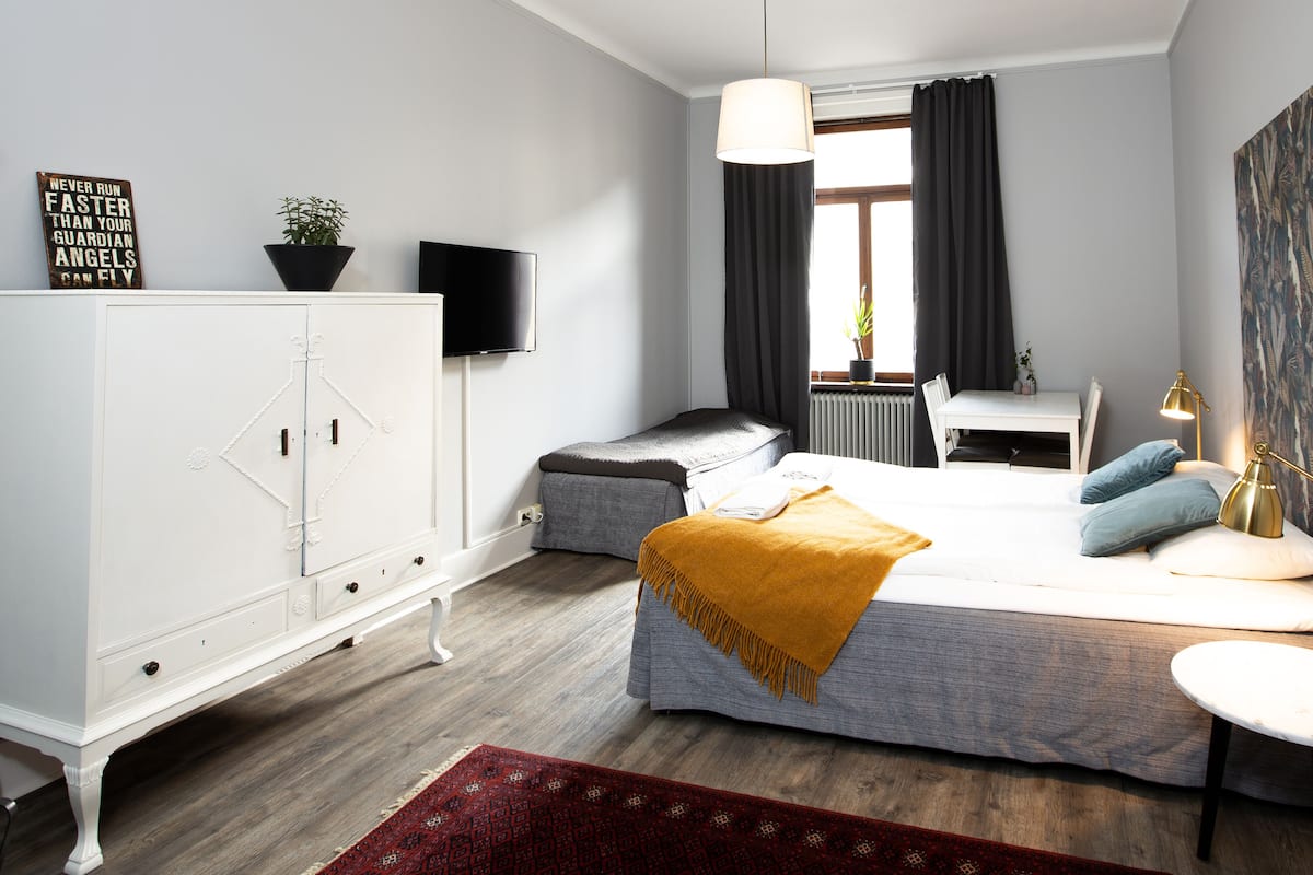 A bedroom with a bed, bedside table, lamp, and a TV on a cabinet.