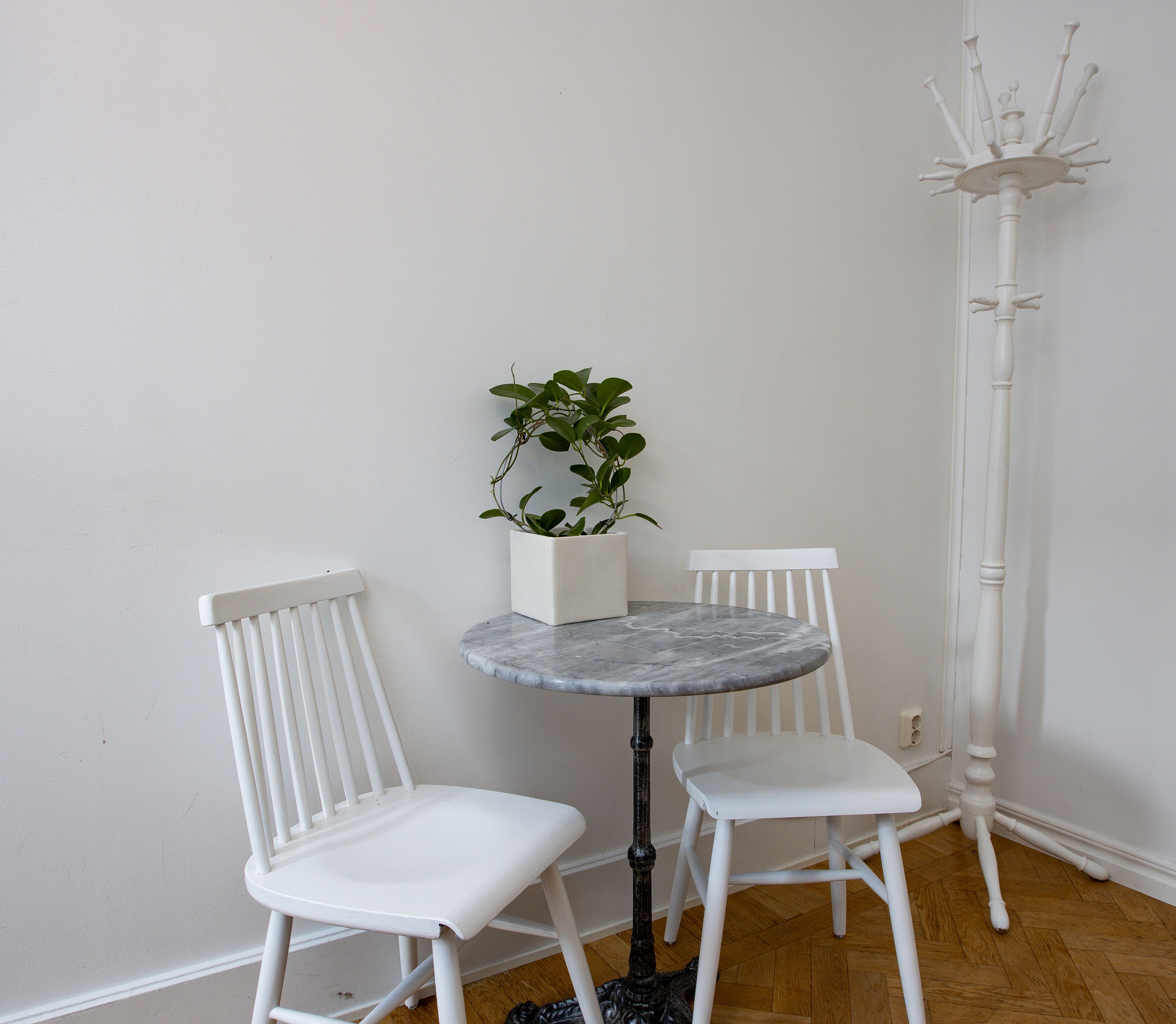 Et lille spiseområde med et rundt bord og to hvide stole, en potteplante og en høj, hvid gulvlampe.