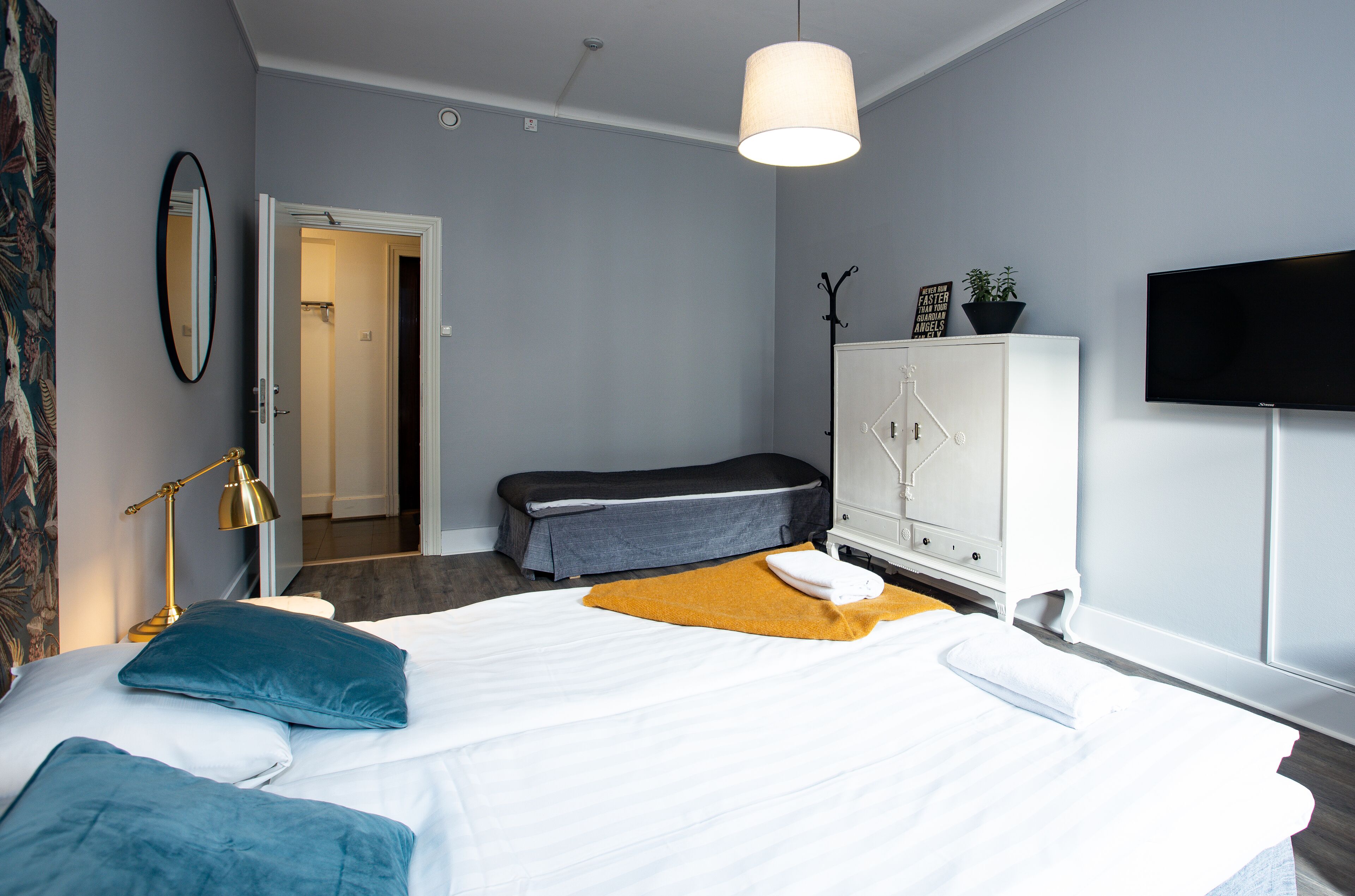 A modern hotel room with a large bed, a bedside lamp, a television, and a wardrobe.