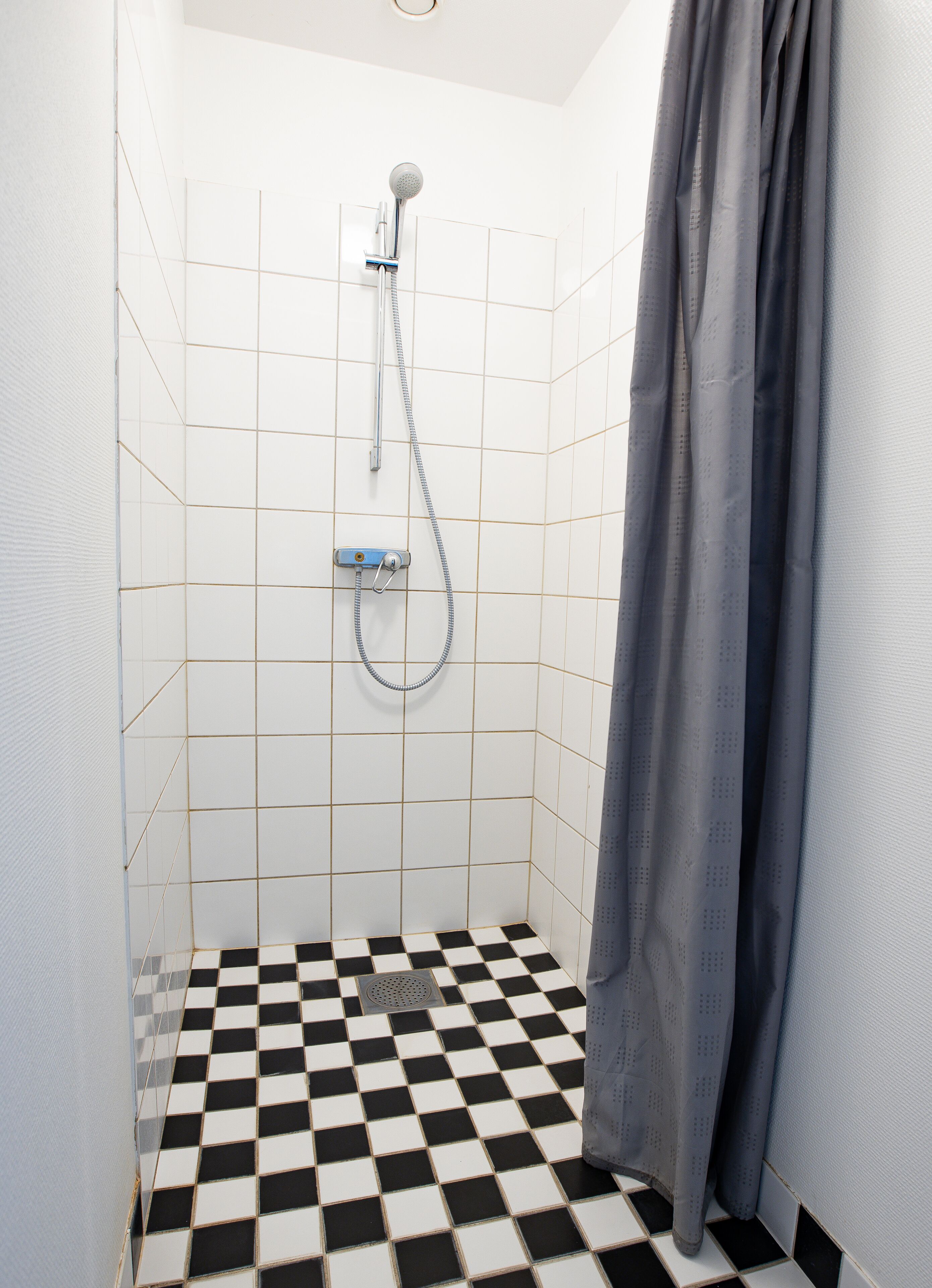 Un baño pequeño con azulejos, una ducha, piso a cuadros y una cortina.
