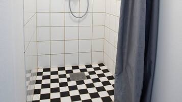 Un baño pequeño con azulejos, una ducha, piso a cuadros y una cortina.