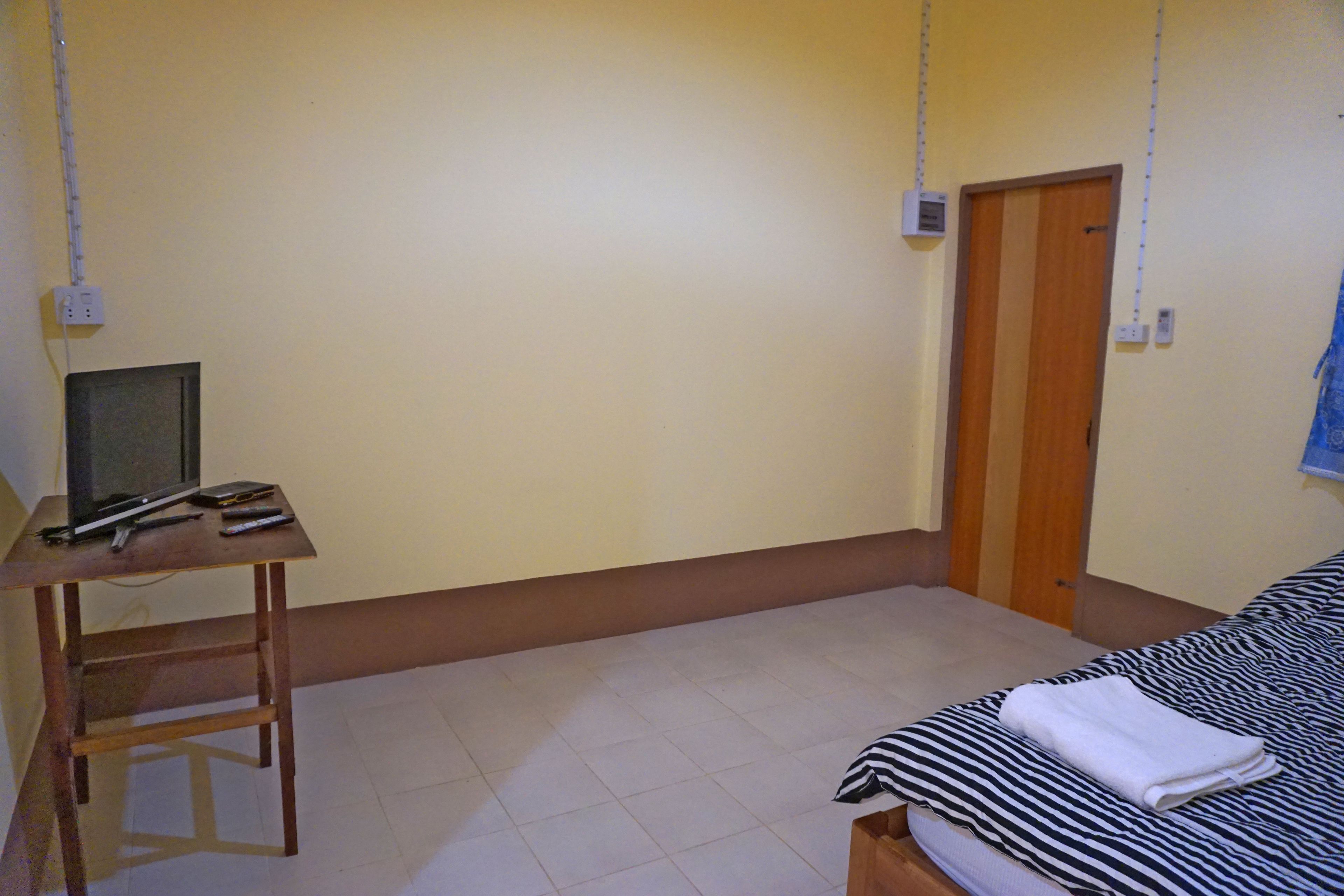 A bedroom with a bed, a desk with a computer, and a door.