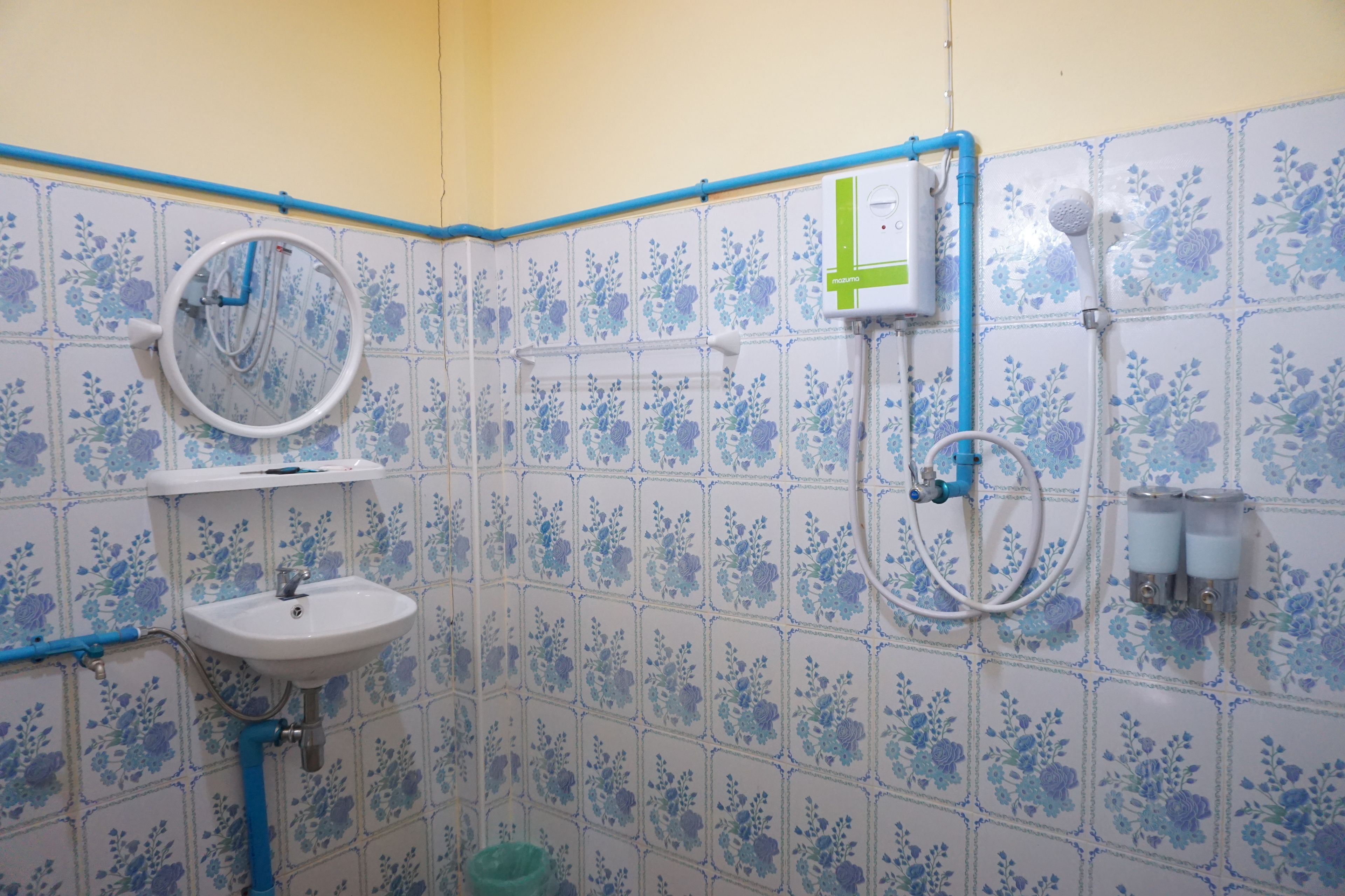 A bathroom with a sink, mirror, shower, and floral-patterned tiles.