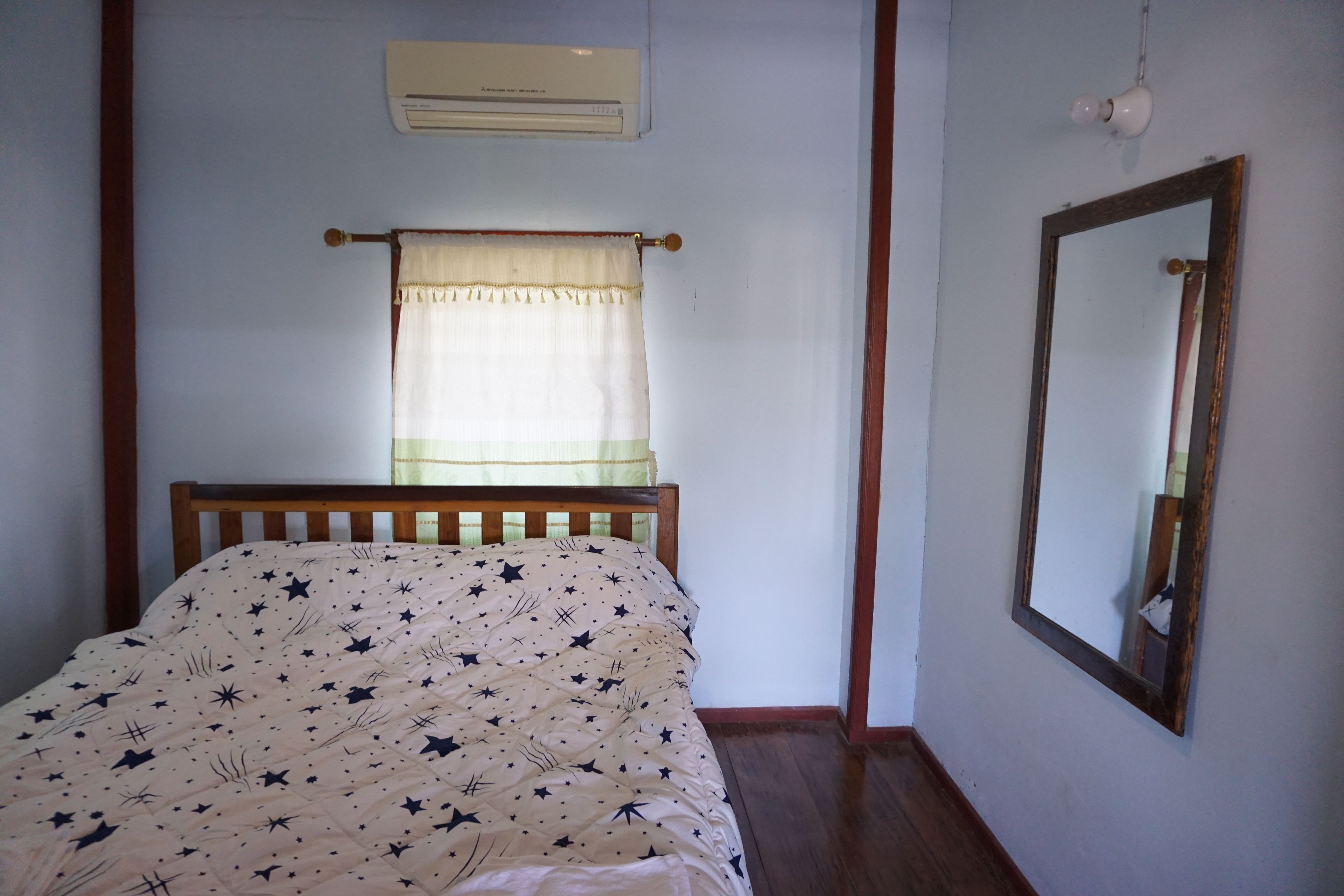 Un dormitorio con cama, ventana con cortina, aire acondicionado de pared y un espejo.