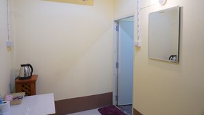 Pieni huone, jossa on valkoinen ilmastointilaite, peili, ovi ja pieni pöytä, jonka päällä on vedenkeitin ja violetti matto.