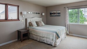Un dormitorio con una cama grande, lámparas de noche, una mesita de noche, una ventana con cortinas y una obra de arte colgada en la pared.