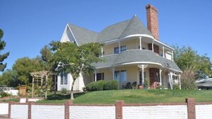 Una casa de dos pisos con un porche envolvente, una chimenea y un muro de contención de ladrillo.