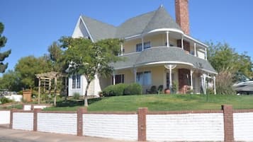 A two-story house with a wrap-around porch, a chimney, and a brick retaining wall.