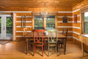 L’intérieur d’un chalet en bois, avec une table et des chaises, un lustre et une vue sur l’extérieur.