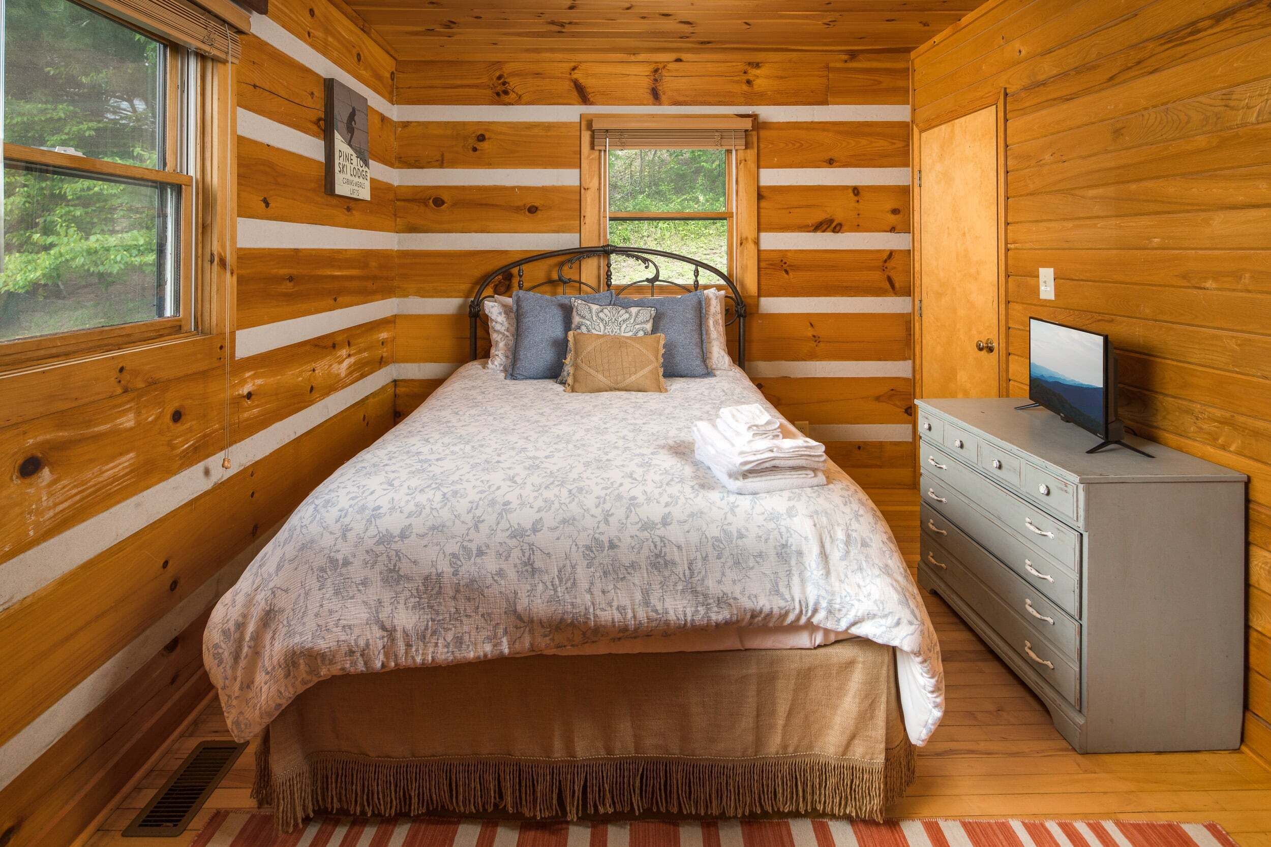 A wooden cabin bedroom with a bed, a dresser, and a window.