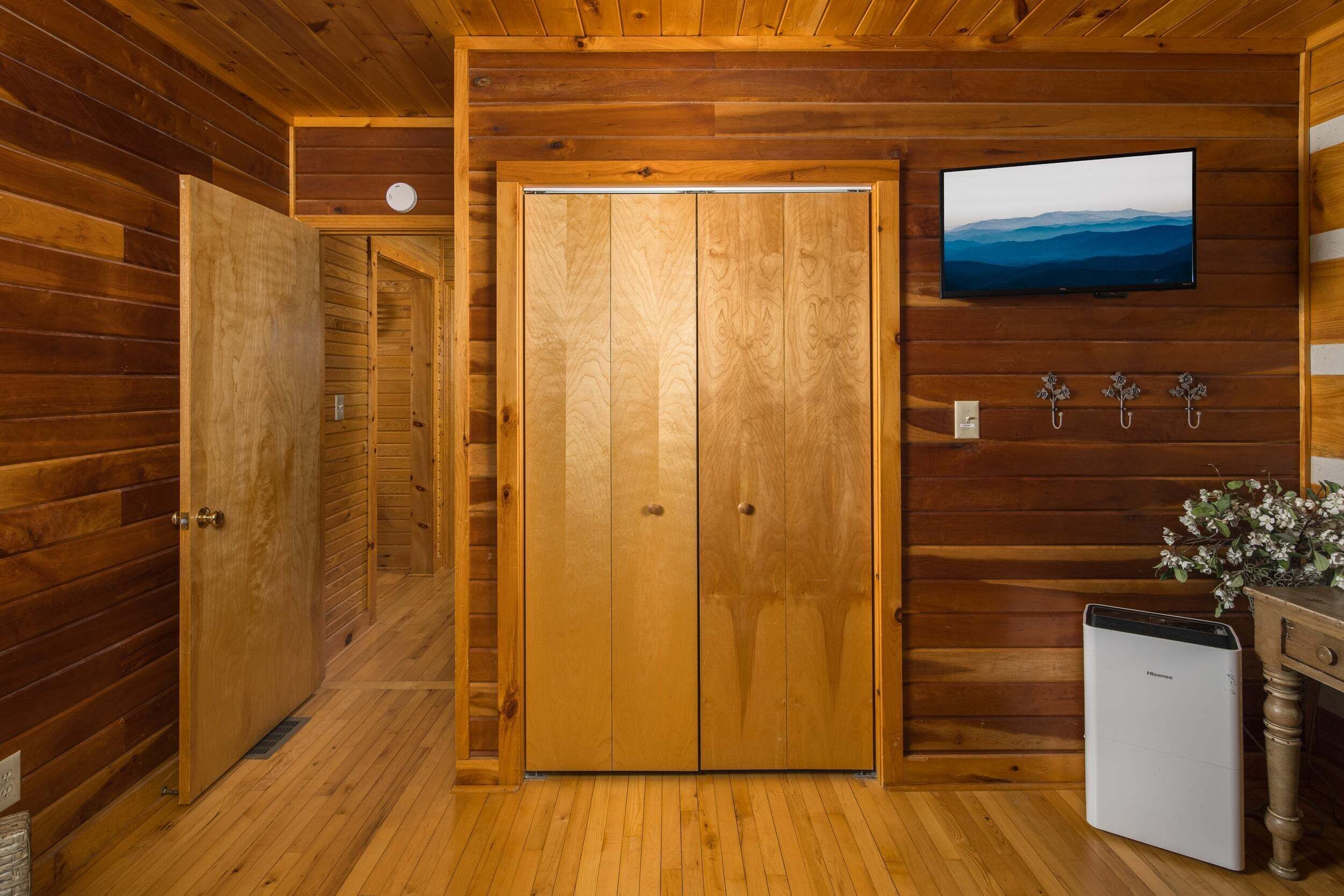 A wooden interior with a double door, a small refrigerator, a television on the wall, and a clock.