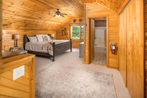 Une chambre dans une cabane en bois, avec un lit, une table de chevet, une lampe et un ventilateur de plafond.