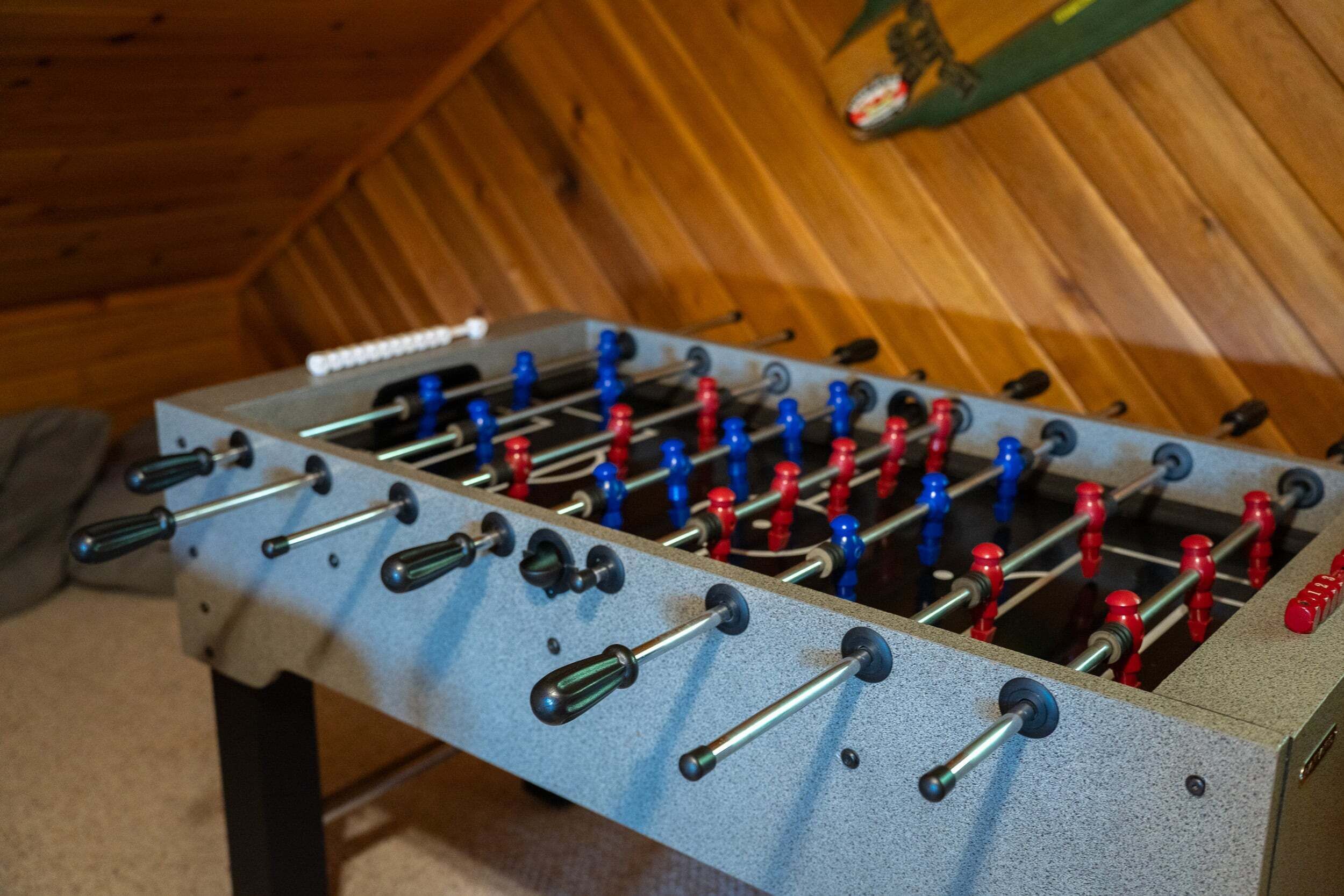 A foosball table with red and blue figures, set against a wooden wall.