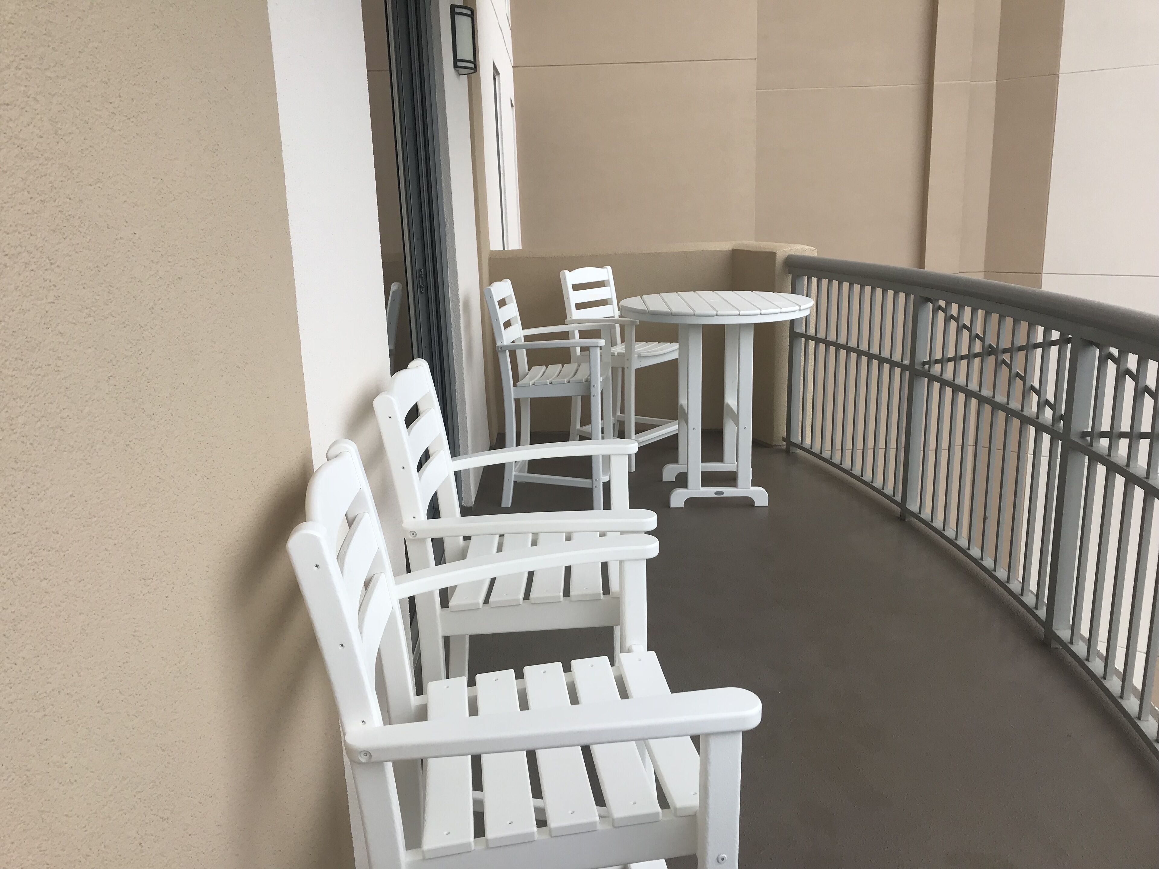 Ein Balkon mit weißen Gartenmöbeln, darunter Bänke und ein Tisch, und einem Metallgeländer.