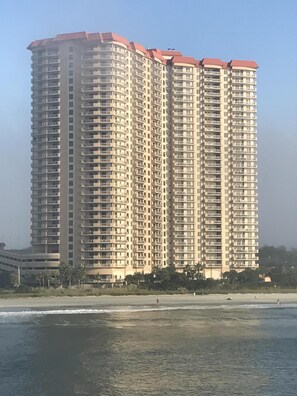 A high-rise building with multiple balconies, located near a beach.
