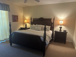 Une chambre à coucher avec un lit à baldaquin, deux tables de chevet avec des lampes, un tableau encadré au mur et une fenêtre avec des rideaux.