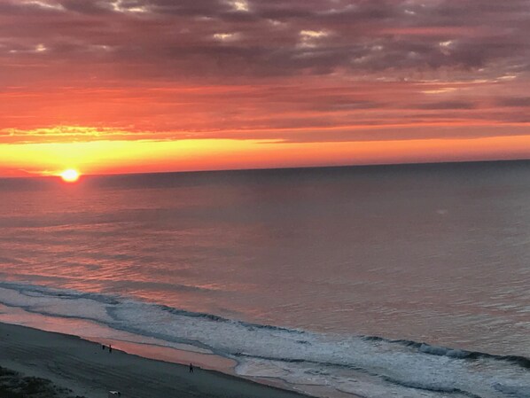 Un coucher de soleil sur l’océan, avec une plage au premier plan.
