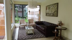 Uma sala de estar com uma mesa de centro de vidro, duas poltronas, um sofá de couro escuro, um candelabro e um quadro da Torre Eiffel.