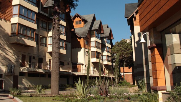 A row of modern multi-story buildings with balconies, surrounded by a landscaped garden with various plants and a large tree. - Gramado me Aptos de Luxo Via Florida (Gramado)