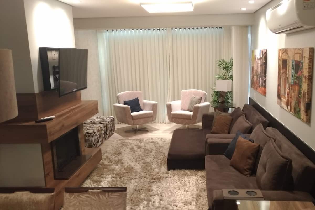 Ein Wohnzimmer mit Fernseher, zwei Sesseln, einer Couch und einem Couchtisch sowie einem Teppich.