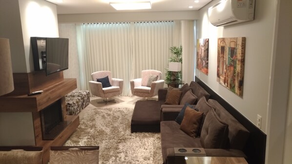 Uma sala de estar com televisão, duas poltronas, um sofá e um tapete.