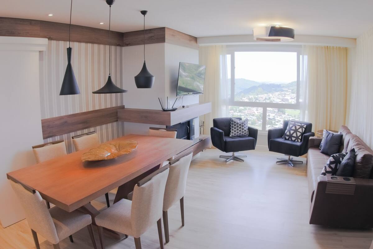 Ein modernes Wohnzimmer mit einem Holzespeisetisch, schwarzen Stühlen, einem schwarzen Sofa und einem großen Fenster mit Blick auf die Stadt.