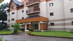A multi-story building with a central entrance, balconies, and a landscaped garden area.