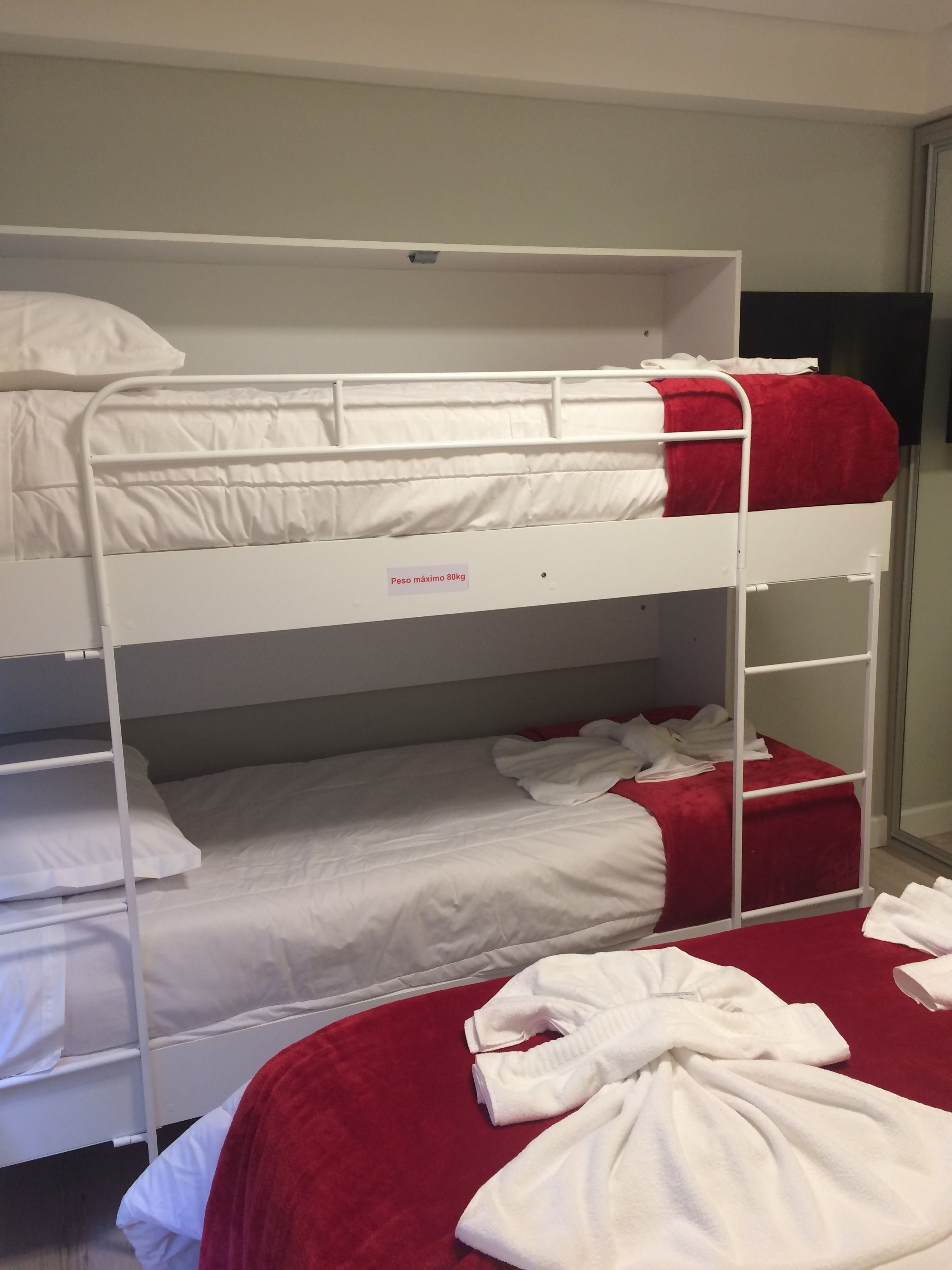 A bunk bed with a maximum weight limit sign, white bedding, and a red blanket.