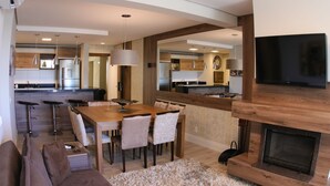 A modern kitchen with a dining area, a fireplace, and a TV mounted on the wall. - Gramado me Aptos de Luxo Via Florida (Gramado)